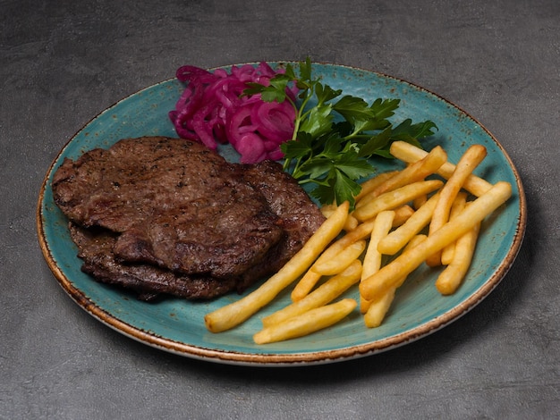 Chuleta de ternera con patatas fritas aderezada con cebolla roja y hierbas