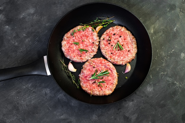 Chuletas de bistec de hamburguesa de carne de res cruda en la sartén sobre la mesa negra.