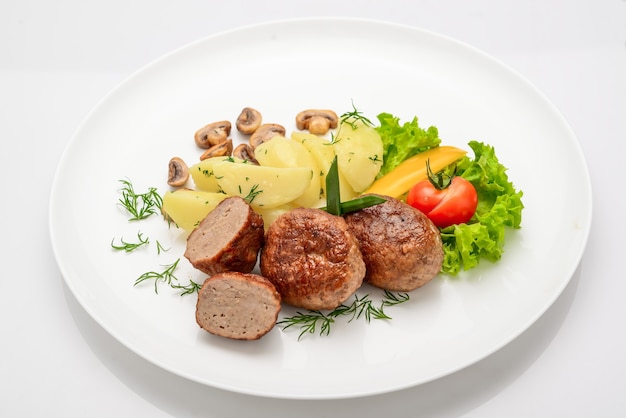 Chuletas caseras con patatas y verduras sobre un fondo blanco.