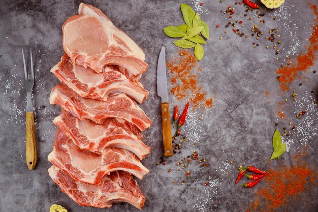 Chuletas de cerdo crudas con hueso con especias sobre fondo oscuro. Vista superior.