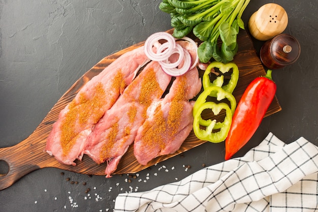 Chuletas de cerdo listas para freír de carne de granja en una tabla de cortar de madera con especias para hornear. fondo negro. vista superior.