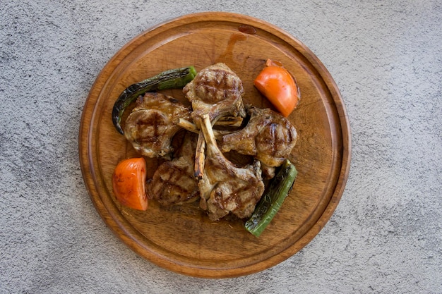 Chuletas de cordero a la barbacoa sobre fondo de madera con pimientos asados tomates y cebollas