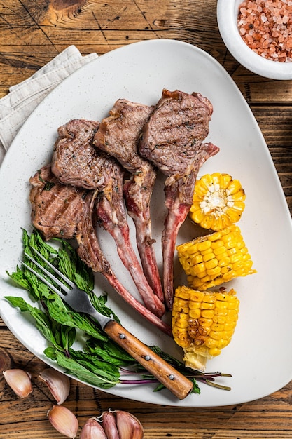 Chuletas de cordero a la plancha en un plato con elote y tomate. fondo de madera. Vista superior.