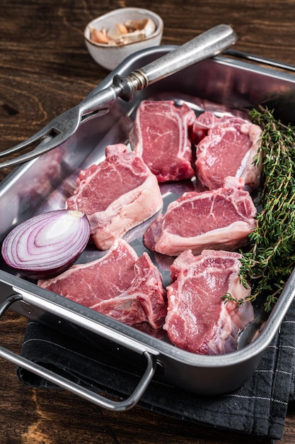 Chuletas de lomo de cordero crudas sin cocer silla de montar en bandeja de cocina con hierbas Fondo de madera Vista superior