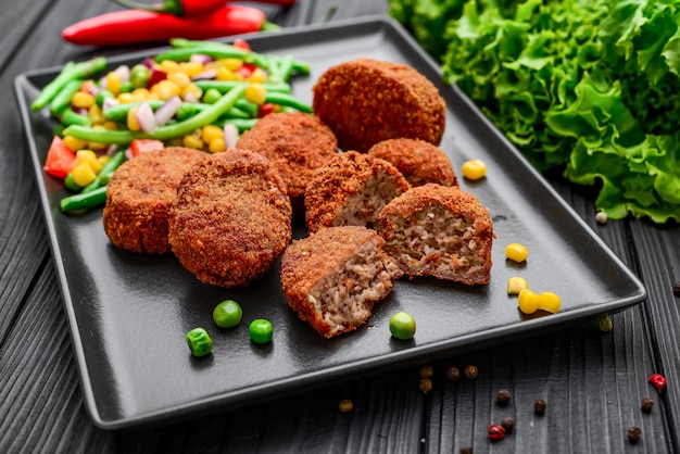 Chuletas de pollo rebozadas con risotto y verduras, sobre una superficie negra