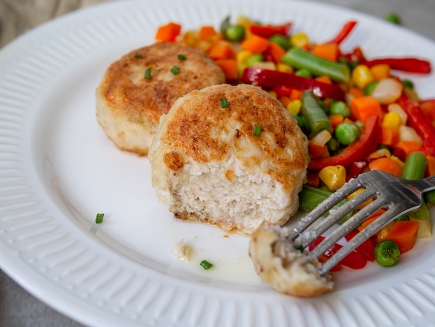 Las chuletas del pollo con las verduras cocidas al vapor de la mezcla, albóndigas del pollo en la placa blanca.