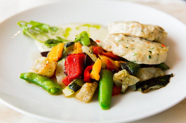 Chuletas de pollo con verduras en plato blanco en mesa blanca en el restaurante