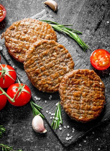 Chuletas en un tablero de piedra con tomates y ajo