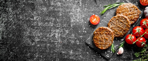 Chuletas en un tablero de piedra con tomates y ajo