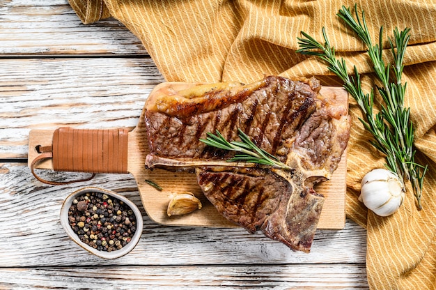 Chuletón de buey a la parrilla sobre una tabla de cortar. Chuletón de res cocido. Espacio de madera blanca. Vista superior