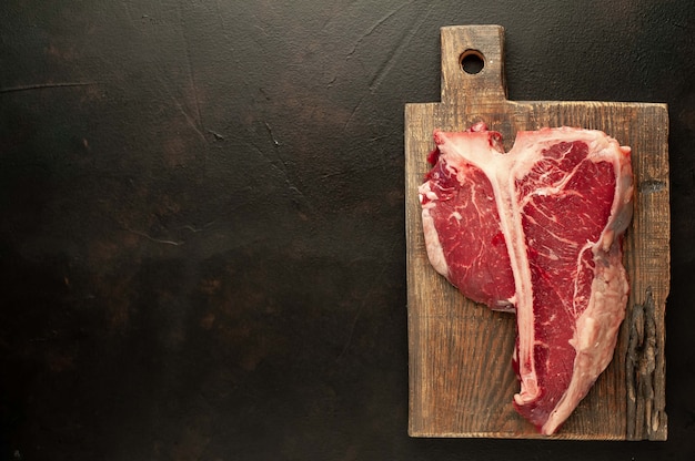 Chuletón crudo con hierbas frescas sobre un fondo de hormigón o pizarra, vista superior, lugar para texto,