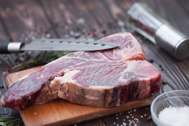 Foto chuletón crudo con romero, pimienta y aceite de oliva en una tabla de cortar preparada para cocinar