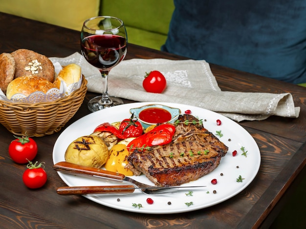 Chuletón de ternera con verduras a la parrilla y una copa de vino tinto en una mesa de restaurante vista lateral