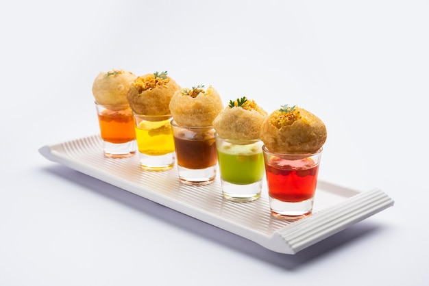 Chupito Panipuri o Golgappa Shots de diferentes sabores de agua servidos en vasos pequeños con un bocadillo de entrada indio puri relleno