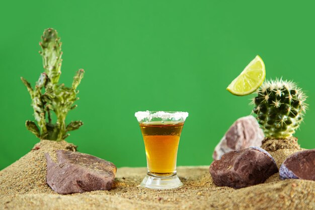 Foto chupito de tequila mexicano con limón y sal entre dunas de arena y cactus fondo verde