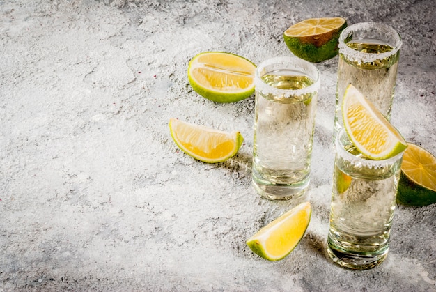 Chupitos de tequila con lima y sal marina sobre una mesa de piedra gris