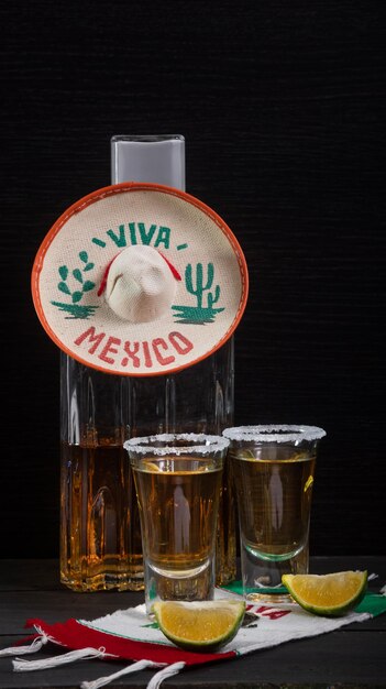 Chupitos de tequila mexicano acompañados de una botella cuadrada de lujo sobre una mesa de madera con limones