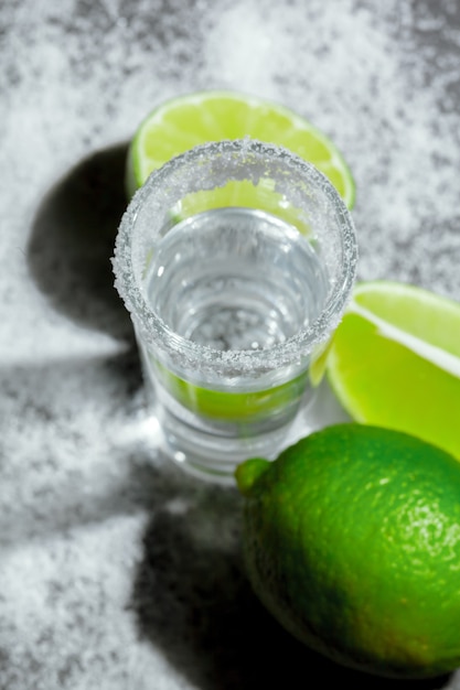 Chupitos de tequila plateado con rodajas de limón y sal sobre tabla de madera