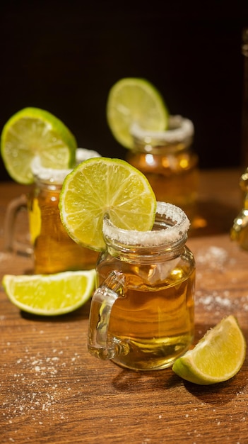 Chupitos de tequila servidos en frascos con sal y limón sobre mesa de madera
