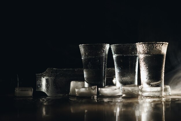 Chupitos de vodka con hielo en el cuadro negro, espacio de copia