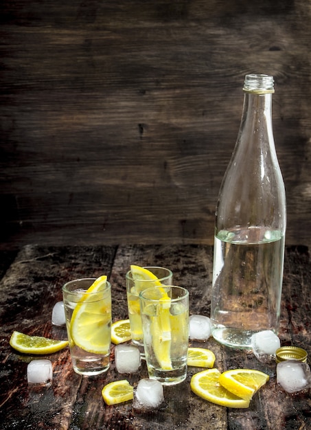 Chupitos de vodka con hielo y limón. Sobre un fondo de madera.