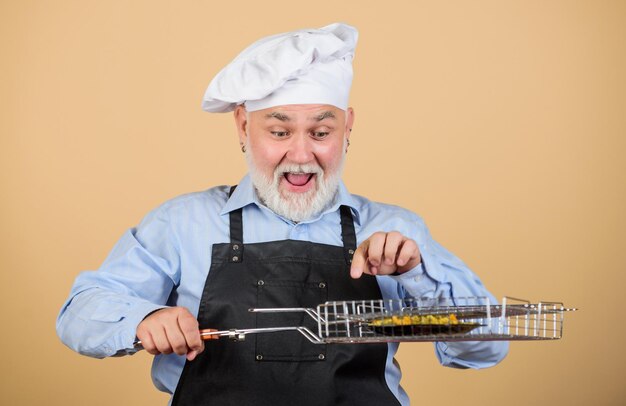 Churrasco com perfeição prefere comida grelhada Piquenique e churrasco Regras da cozinha prepare o jantar para a família Fim de semana da família homem sênior com chapéu de chef cozinhar homens com barba utensílios de cozinha para churrasco