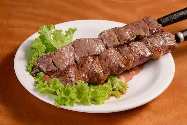 Churrasco de carne em espetos Kebab brasileiro tradicional em chapa branca na mesa de madeira