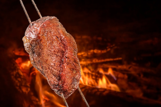 Churrasco de picanha grelhada com fogo desfocado ao fundo Também chamado de churrasco