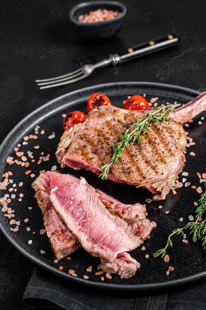 Churrasco em fatias de costela de bife Tomahawk em um prato com sal rosa. Fundo preto. Vista do topo.