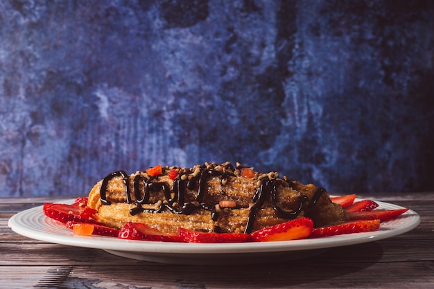 Churros con almendras trituradas con chocolate y fresas en un plato blanco