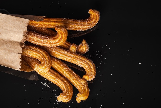 Churros azucarados en mesa negra con reflejo. Churros en bolsa de papel.