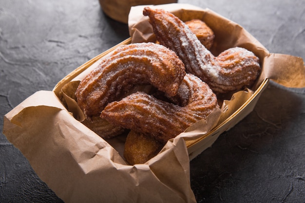 Churros en una bolsa de papel con salsa de azúcar y chocolate sobre negro