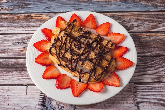 Churros con chocolate y fresas en un plato blanco.