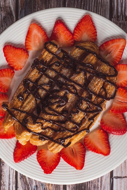 Churros con chocolate y fresas en un plato blanco.