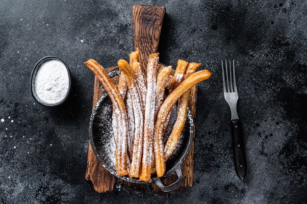 Churros de sobremesa mexicana tradicional com açúcar em pó em uma panela. fundo preto. vista do topo.