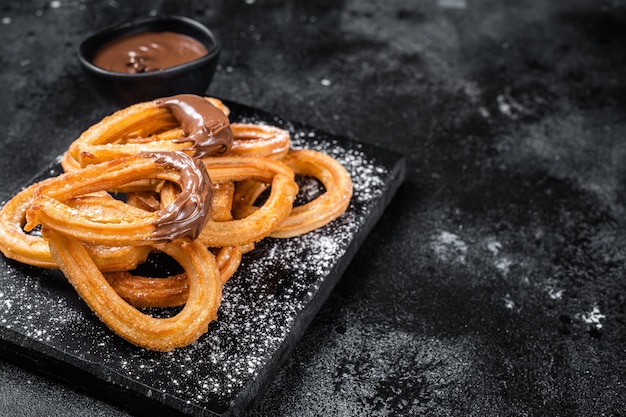 Churros de sobremesa mexicana tradicional com molho de chocolate. Fundo preto. Vista do topo. Copie o espaço.