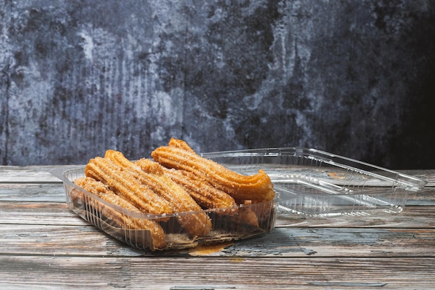 Churros em um recipiente de plástico em uma mesa de madeira