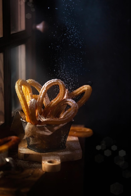 Churros espanhóis tradicionais em cima da mesa. Foto escura e temperamental, estilo rústico. Luz mágica sai da janela