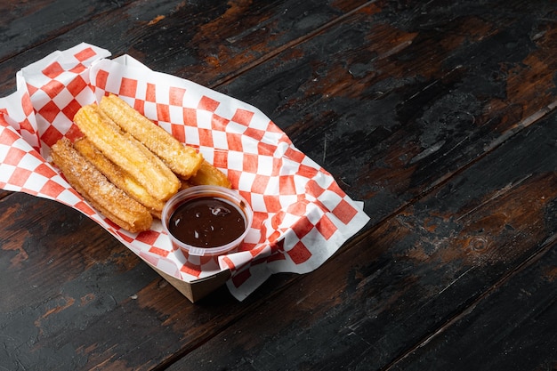 Churros mit Zuckerpulver, in der Box im Papierfach, auf altem dunklem Holztischhintergrund mit Platz für Text, Copyspace