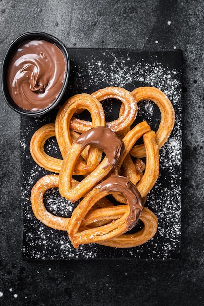 Churros de postre tradicional mexicano con salsa de chocolate Fondo negro Vista superior