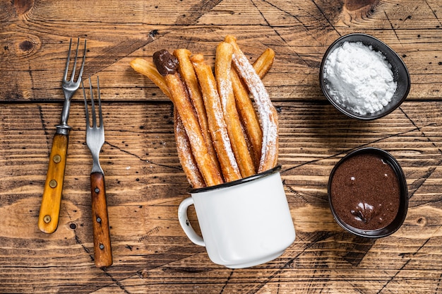 Churros con salsa de azúcar y chocolate. fondo de madera. Vista superior.