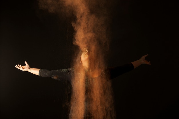 Foto chuva de poeira laranja sobre uma mulher indiana dançando no festival de holi