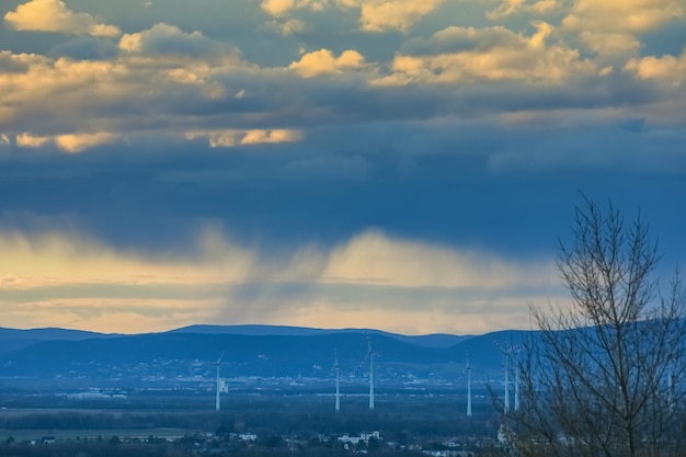 Chuva forte sob nuvens durante o pôr do sol em uma paisagem com moinhos de vento