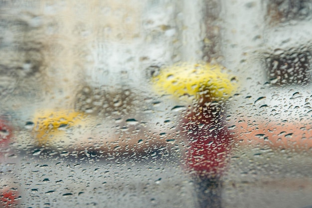 Chuva molhada cai na mulher de vidro com silhueta amarela através de vidro molhado