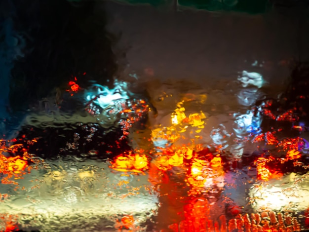 Chuva turva cai na janela do carro com bokeh de luz de estrada no fundo abstrato da estação chuvosa