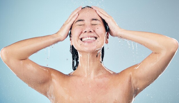 Foto chuveiro de mulher feliz e gotas de água na higiene, lavagem ou preparação contra um fundo de estúdio azul pessoa feminina sorri em relaxamento, limpeza de lavagem corporal ou rotina de cuidados com a pele sob chuva no banheiro