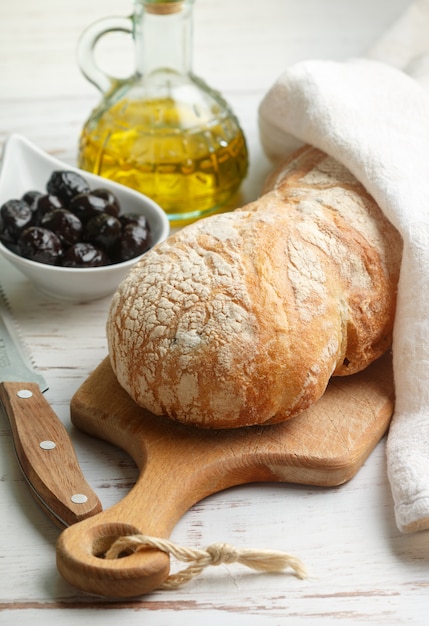 Ciabatta con aceitunas, fresco delicioso pan italiano tradicional, aceitunas y aceite de oliva en una mesa de madera blanca