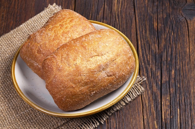 Ciabatta-Brot mit zwei Laiben in der Platte auf dunklem hölzernem Hintergrund Beschneidungspfad eingeschlossen