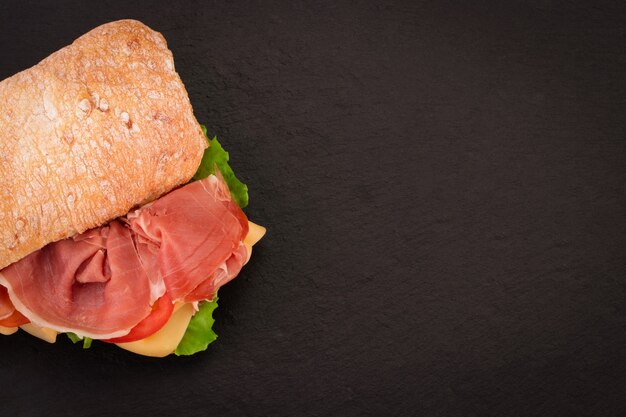 Ciabatta-Sandwich mit Salat, Schinken und Käse über Steinhintergrund. Draufsicht mit Kopienraum.