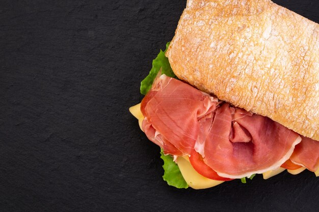 Ciabatta-Sandwich mit Salat, Schinken und Käse über Steinhintergrund. Draufsicht mit Kopienraum.